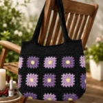 Handgemachte Häkeltasche Viola Schwarz Lila Gelb von Elly Living mit Granny-Square-Muster auf Holzstuhl