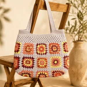 Handgemachte Häkeltasche Aurina Creme Apricot Bordeaux von Elly Living mit buntem Granny-Square-Muster auf Holzstuhl