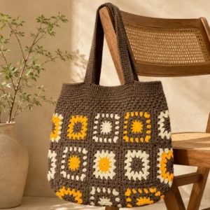 Home Handgemachte Häkeltasche Mokka Braun Gelb Creme von Elly Living mit Granny-Square-Muster auf Holzstuhl